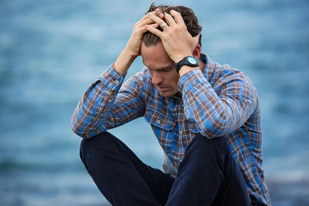 A man sits on the ground, head in hands, visibly distressed, possibly experiencing a headache from Rad 140 use.